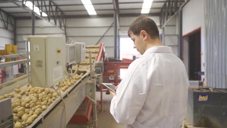 Food-engineer-working-on-tablet-in-potato-packaging,-storage-factory.